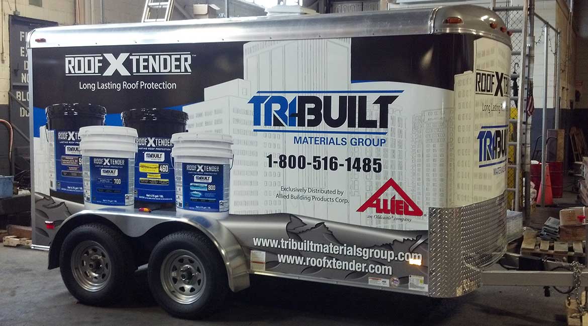 An S.A.B. Graphics installer squeegeeing a printed vinyl panel onto the side of an enclosed trailer.